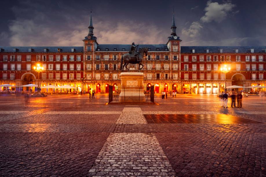<strong>Plaza Mayor – <a href="https://preprod.viagemeturismo.abril.com.br/cidades/madri/" target="_blank" rel="noopener">Madri</a> – <a href="https://preprod.viagemeturismo.abril.com.br/paises/espanha/" target="_blank" rel="noopener">Espanha</a></strong> Boa parte das cidades espanholas e mesmo aquelas fundadas e conquistadas por eles nas Américas têm sua <strong>Plaza Mayor</strong>. Centro gravitacional da vida cívica, mercado e sede de edifícios governamentais, tudo girava ao seu redor. A mais bela e definitiva dessas praças não poderia estar em outro lugar, senão na capital do país. Ao longo de sua história, a Plaza Mayor de Madri foi palco de touradas, execuções e autos de fé da radical Inquisição espanhola, um local onde igreja e coroa atestavam seu poder perante o povo. O formato retangular e a relativa simetria no desenho dos edifícios é obra de sucessivos monarcas, mas boa parte das atuais características se devem a Filipe III, cuja estátua está fixada no centro da praça. Cafés e restaurantes espalham sob as arcadas centenas de mesas durante o dia, um ótimo lugar para ver a vida passar  <em>Busque hospedagem em Madri</em>