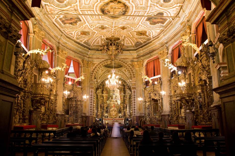 <strong>9. Matriz de Nossa Senhora do Pilar e Museu de Arte Sacra </strong><strong>–</strong><strong> Ouro Preto</strong> A incrível quantidade de ouro dos altares da Matriz de Nossa Senhora do Pilar, em Ouro Preto – são mais de 400 quilos – e a riqueza de detalhes dos retábulos são os exemplos máximos do barroco brasileiro, com entalhes das três fases do estilo artístico. Nos seis altares laterais estão representadas cada uma das irmandades e grupos sociais da época. O <strong>Museu de Arte Sacra</strong>, no subsolo da sacristia, exibe imagens de Nossa Senhora do Pilar, Santa Bárbara e Nossa Senhora da Conceição. Preste atenção no efeito óptico causado pela figura do Cordeiro de Deus, no teto: um dos braços da cruz parece mudar de lado na medida em que você caminha <a href="https://www.booking.com/city/br/ouro-preto.pt-br.html?aid=332455&label=viagemabril-13-atracoes-historicas-mg" target="_blank" rel="noopener"><em>Reserve agora o seu hotel em Ouro Preto (MG)</em></a>