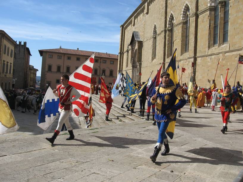 <strong>AREZZO</strong> (a 81 km de Montalcino)        Em <strong><a href="https://viajeaqui.abril.com.br/cidades/italia-arezzo" rel="Arezzo " target="_blank">Arezzo</a></strong>, você receberá um verdadeiro banho de arte – de fato a cidade está incluída entre as chamadas Cidades da Arte.        De origem etrusca, como a maioria das cidades toscanas, hoje é constituída de uma parte moderna e de um centro histórico ainda em grande parte cercado por muralhas que protegem seu patrimônio artístico.        No passado foi célebre pela produção de cerâmica artística, especialmente os famosos vasos aretinos. A colina do <em>Duomo</em> domina a cidade embelezada pelo jardim público conhecido como <em>Passeggio del Prato</em> (Passeio no Prado) – herança da época áurea do domínio da mais famosa família florentina: os Medici.        Até hoje mantém uma tradição popular originária da Idade Média: a <a href="https://www.giostradelsaracino.arezzo.it" rel="Giostra del Sarracino" target="_blank"><em>Giostra del Sarracino</em></a>.O evento se realiza em duas datas todos os anos<em>: Giostra di San Donato</em> em 23 de junho, <em>e Giostra della Madonna del Conforto</em> em 2 de setembro.        Para fechar com chave de ouro o seu itinerário pela Toscana, nada melhor do que esta parada em Arezzo para admirar a <em>Piazza Grande</em> e o seu conjunto arquitetônico perfeito, que inclui a Loggia Vassari, cuja fachada foi criada por Giorgio Vassari, a igreja de San Domenico – para admirar um crucifixo de autoria do pintor Cimabue –, a Chiesa di San Francesco, que conserva os esplendidos afrescos de Piero della Francesca e a Pieve di Santa Maria, a mais bonita igreja medieval da cidade.        Com o olhar cheio de muita beleza e o doce sabor do bom vinho na boca, você pode voltar para Florença, a apenas 73 quilômetros de Arezzo. <em>Arrivederci a presto!</em>