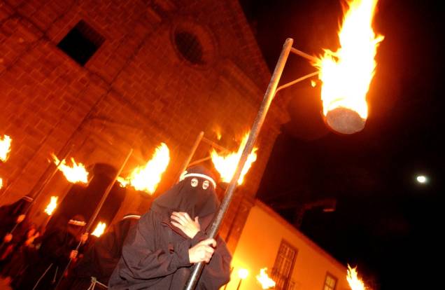 Um farricoco (fiel encapuzado) carrega uma tocha durante a Procissão do Fogaréu, em Guimarães, Portugal. A celebração dramatiza a perseguição e prisão de Cristo, às 0h da quinta-feira santa Um farricoco (fiel encapuzado) carrega uma tocha durante a Procissão do Fogaréu, em Guimarães, Portugal. A celebração dramatiza a perseguição e prisão de Cristo, às 0h da quinta-feira santa