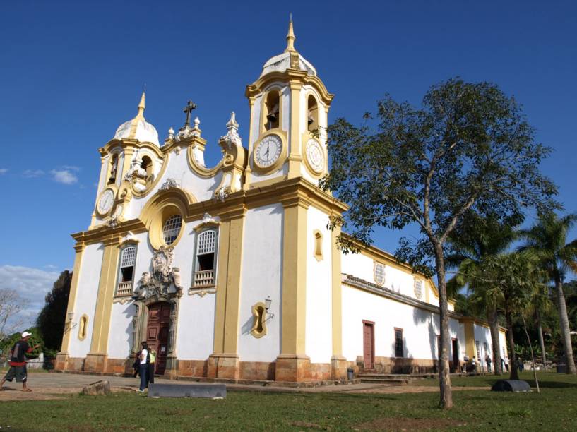 <strong>1. Igreja Matriz de Santo Antônio </strong>–<strong> Tiradentes</strong> Um dos mais ricos exemplares do barroco brasileiro, a Matriz de Santo Antônio, na cidade de Tiradentes, foi construída com a frente voltada para a Serra de São José. Logo na entrada, é difícil não se impressionar com os lustres de prata e a quantidade de ouro que decora o altar e suas imagens. As esculturas da fachada e da portada são atribuídas a Aleijadinho e datam de 1810. No alto, o órgão português de 1788 tem oito fileiras de tubos e belíssimas pinturas em estilo rococó. Também há opção de visitá-la à noite: o Roteiro Narrado conta a história da igreja com jogos de luz e um texto de 16 minutos gravado pelo ator Paulo Goulart; em seguida, a artista Elisa Freixo toca composições clássicas no órgão. Nos feriados prolongados, as irmãs Salomé (que toca flauta) e Amélia (que toca clavinova) costumam apresentar músicas barrocas <a href="https://www.booking.com/city/br/tiradentes.pt-br.html?aid=332455&label=viagemabril-13-atracoes-historicas-mg" target="_blank" rel="noopener"><em>Reserve o seu hotel em Tiradentes (MG)</em></a>