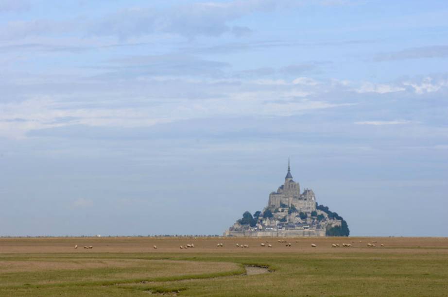 O Mont Saint-Michel em época de maré baixa; a Abadia construída sobre o ponto mais alto do rochedo de granito é a principal atração do local