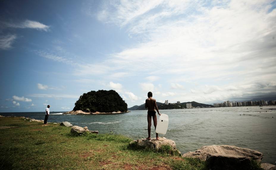 Menino observa as ondas com sua prancha de bodyboard na Praia de José Menino