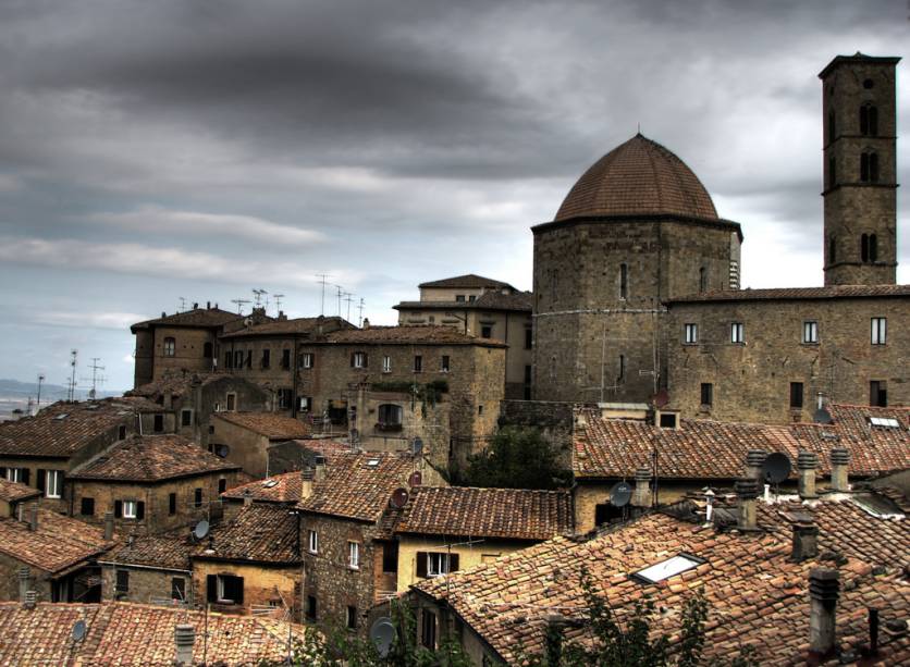 <strong>VOLTERRA </strong>(a 35 km de San Gimigniano)        Por algumas horas esqueça que está na terra dos bons vinhos! Você acaba de chegar à terra dos vampiros! Vampiros?! De pacata e anônima, <a href="https://viajeaqui.abril.com.br/cidades/italia-volterra" rel="Volterra " target="_blank"><strong>Volterra</strong></a> de repente se tornou ponto de peregrinação turística para quem espera encontrar algum membro da família dos <em>Volturi</em>, protagonistas da saga <em>Crepúsculo</em>, de Stephenie Meyer.        A escritora provavelmente se inspirou no antigo nome etrusco dos habitantes da região: <em>Velathri</em> para criar os seus modernos vampiros. Lendas à parte, como todas as cidades medievais da região, suas ruas estreitas e sinuosas e os vestígios de antiguíssimas civilizações, ainda presentes em alguns aspectos, alimentam a imaginação e a fantasia.        Contrastando com o lado sombrio de<strong> Volterra</strong>, os campos ao seu redor são coloridos de amarelo vibrante, cobertos por plantações de girassol que florescem em junho. Não deixe de visitar a <em>Catedrale di Santa Maria Assunta,</em> cuja construção remonta ao início da Idade Média na Piazza dei Priori, e o <a href="https://viajeaqui.abril.com.br/estabelecimentos/italia-volterra-atracao-museo-etrusco-guarnacci" rel="Museo Etrusco Guarnacci" target="_blank"><em>Museo Etrusco Guarnacci</em></a> (Via don Minzoni, 15), que possui um importante acervo de peças etruscas. Se tiver tempo, visite o <a href="https://www.teatroromanovolterra.it" rel="Antico Teatro Romano" target="_blank">Antico Teatro Romano</a> (Parco Archeologico E. Fiumi, +39(588)86150, <a href="mailto:info@teatroromanovolterra.it">info@teatroromanovolterra.it</a>)