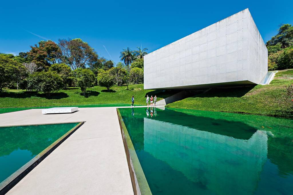 Arte, Inhotim, Brasil Um grande espelho d´água cerca o caminho de pedra até a construção sem janelas e de formato quadrado construída contra um morro, com um terço de sua extensão suspensa.