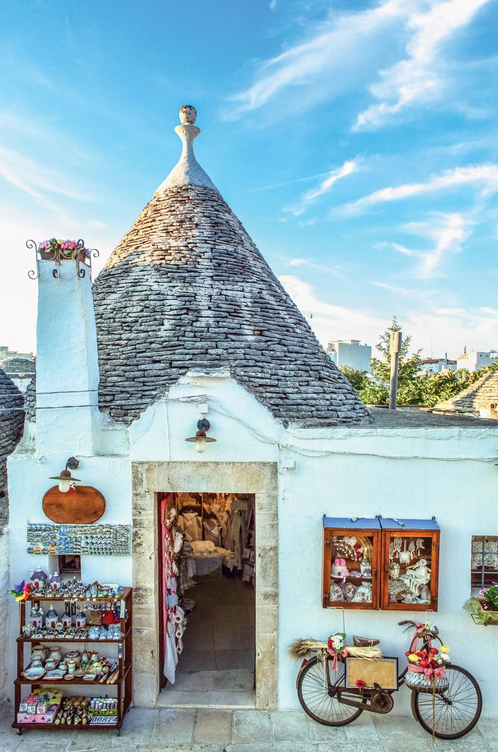 Loja em Alberobello, Puglia, Itália Loja de souvenirs dentro de uma casa em estilo trullo. Do lado de fora, à esquerda da porta, uma prateleira com vários objetos e, à direita, uma bicicleta encostada na parede