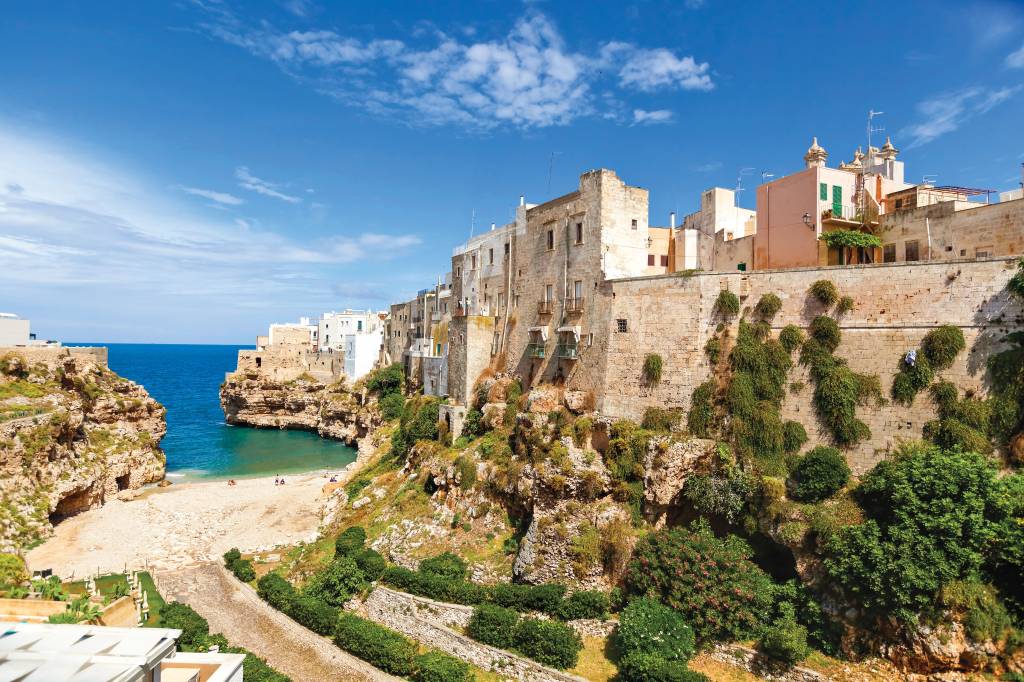 Praia em Polignano a Mare, Puglia, Itália Casas e um grande e alto muro, cercado de plantas, à beira de uma praia e com vista para o mar