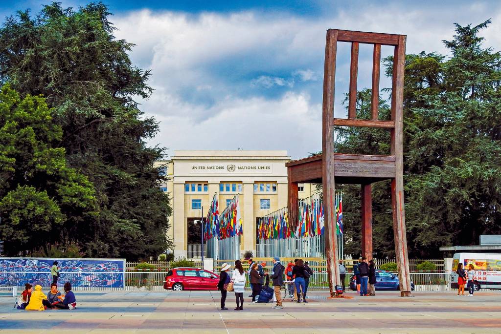 O edifício da ONU, aberto para visitação, com uma enorme escultura de cadeira em primeiro plano, seus pés pousados tanto dentro da propriedade da ONU como fora da grade