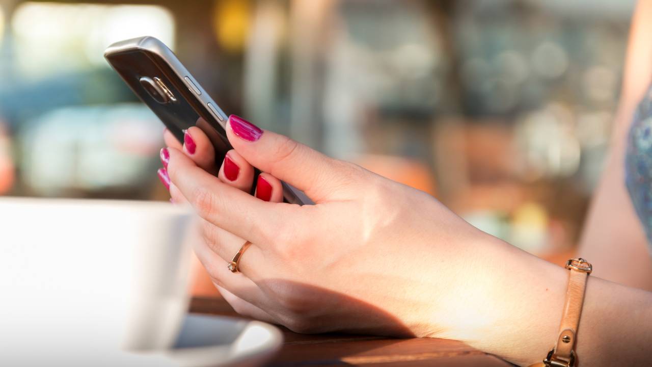 Mãos femininas com celular xícara de café
