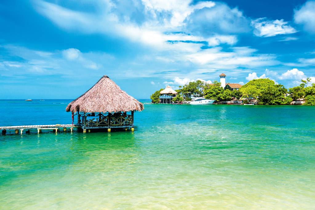 Cabanas em cima do mar claro e abaixo de um céu limpo e ensolarado