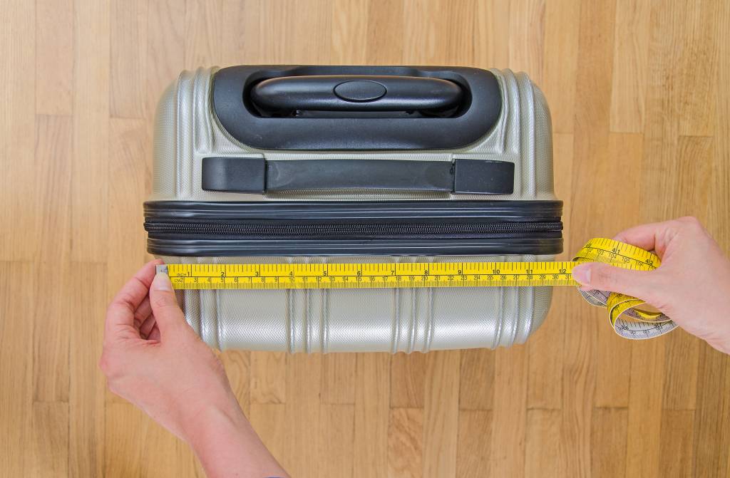 Pessoa mede bagagem de mão com fita métrica Pessoa mede bagagem de mão com fita métrica