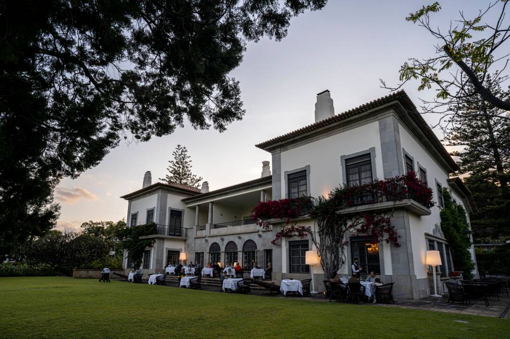 Casarão branco de dois andares com as mesas do restaurante na varanda e no gramado, ao anoitecer