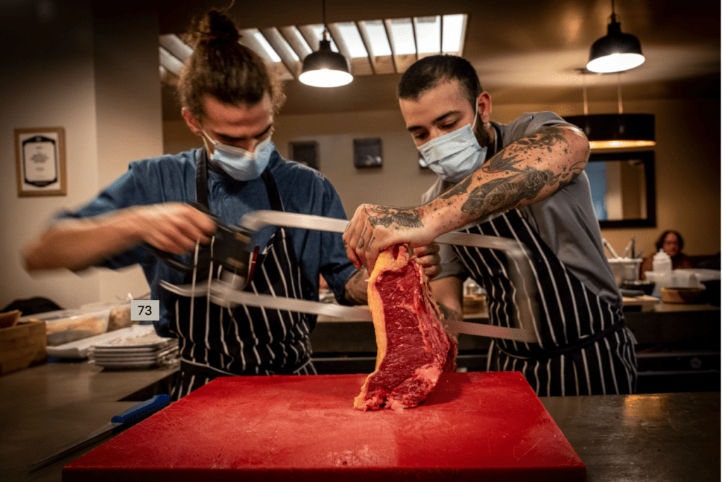 Kampo Dois homens serram um grande pedaço de carne crua com um serrote no balcão de um restaurante na Ilha da Madeira, em Portugal