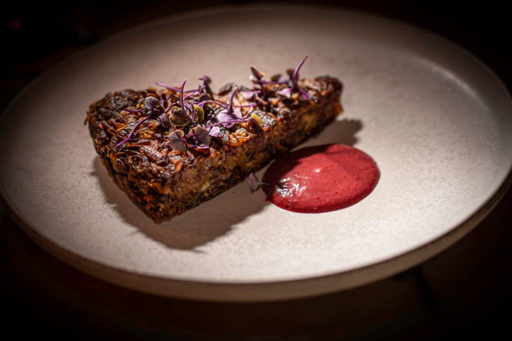 Fatia de barata rosti com flores roxas por cima e um molho vermelho ao lado