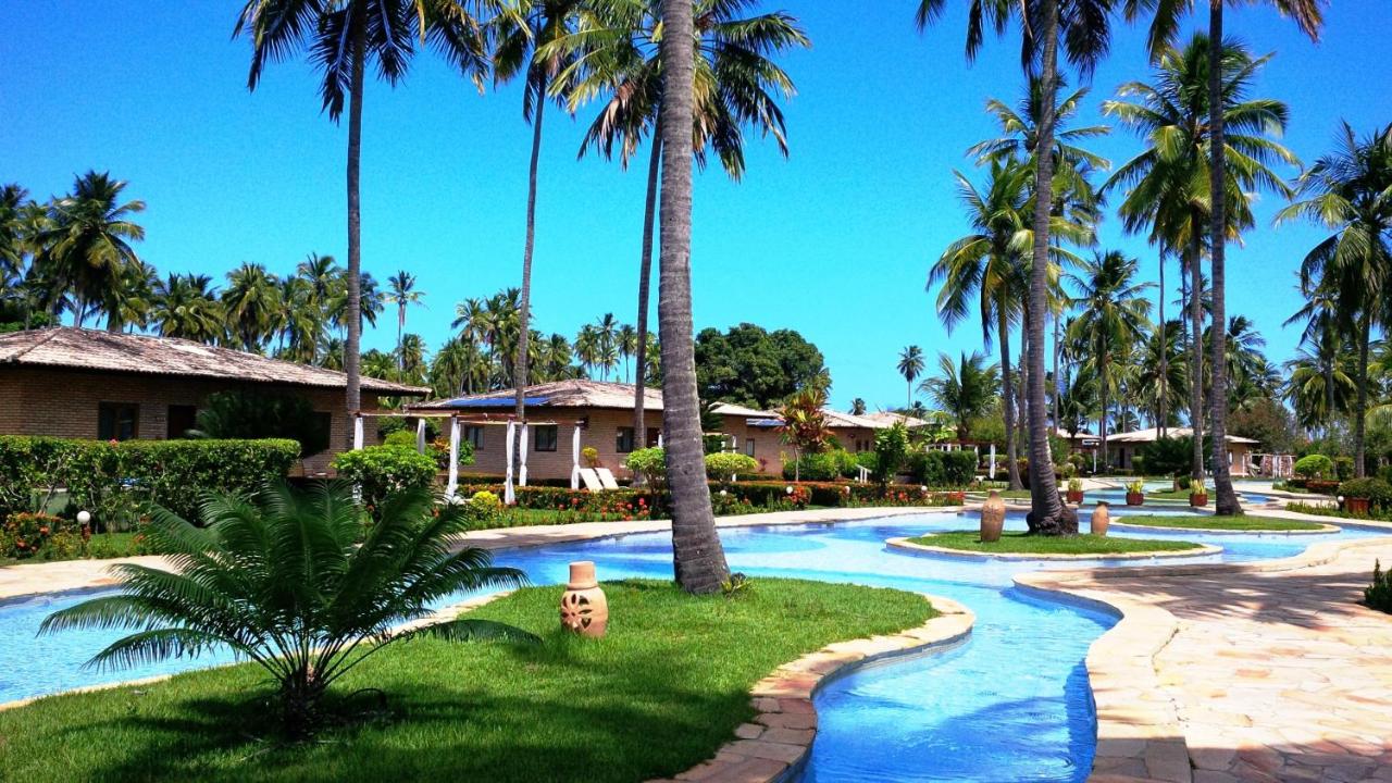 Grand Oca Maragogi All Inclusive Resort A imagem mostra uma piscina que corta uma área de coqueiros e casas em um resort