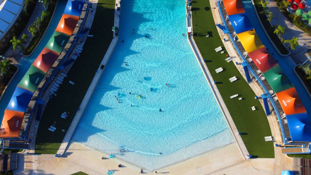 Wet ‘n Wild – Wave Lagoon Drone A imagem mostra um,a piscina de ondas vista de cima. Ao redor da atração, é possível ver tendas de diversas cores.
