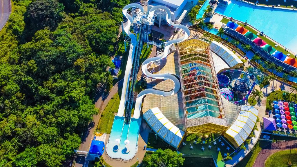 A imagem aérea do parque aquático mostra dois toboáguas grandes, um balcão e um outro brinquedo de escorregar, além de mata verde e tendas coloridas.