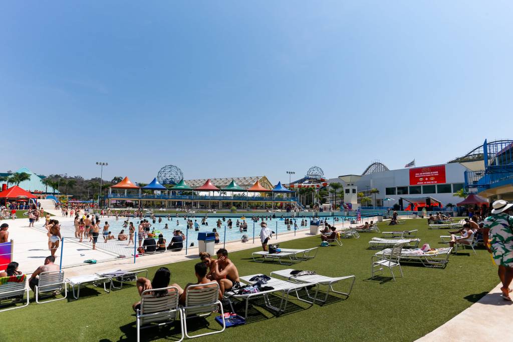 Wet’n Wild – convivência A imagem mostra várias pessoas em espreguissadeiras ao lado de uma piscina de ondas.