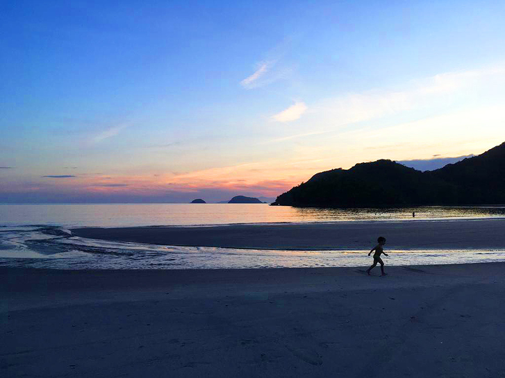 Criança correndo em uma praia com um por do sol rosado ao fundo