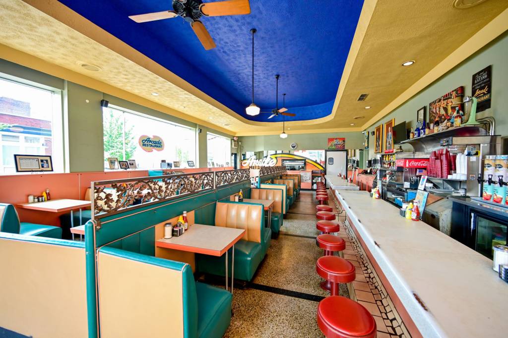 Arcade-Restaurant-BX A imagem mostra o interior de um restaurante antigo com móveis em várias cores, como verde, vermelho, azul e amarelo.