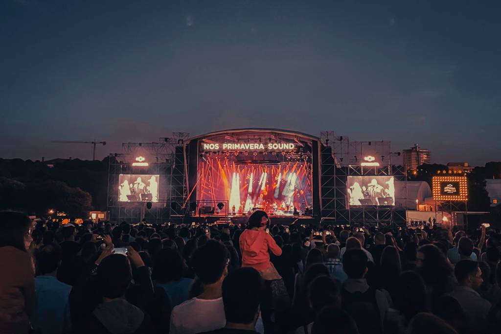 Palco iluminado com luze vermelhas e uma multidão em frente, no show do Nick Cave