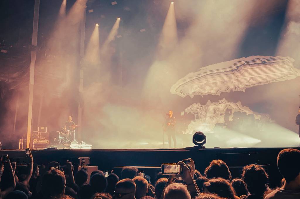 Detalhe de um cantor no palco de um festival de música, com projeções audiovisuais por trás