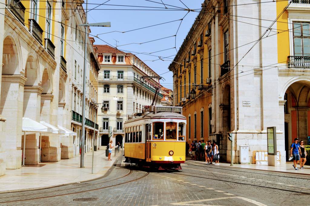 Bonde elétrico amarelo em uma rua calçada de pedras, cercada de prédios baixos de fachadas coloridas