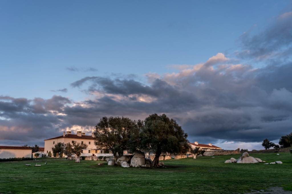 Edifício branco de dois andares com árvores e pedras na frente