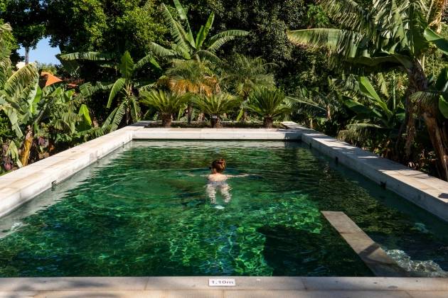 Mulher nadando em uma piscina de águas verdes cercada de bananeiras