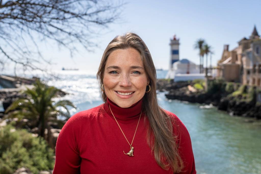 Sissi Freeman, uma mulher loira, de blusa vermelha, fotografada em frente ao mar em Cascais, Portugal