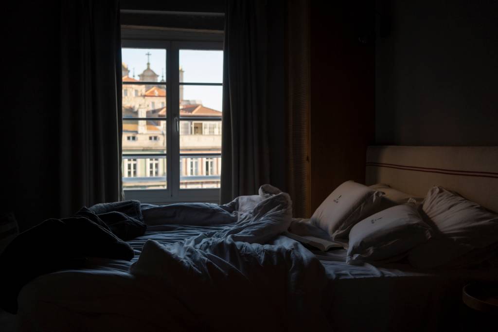 1BB05124 Num primeiro plano, uma cama desarrumada, com uma janela e, do lado de fora, a cidade do Porto