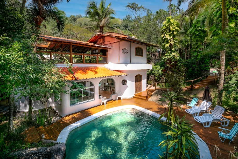 A foto mostra uma casa branca de dois andares com piscina