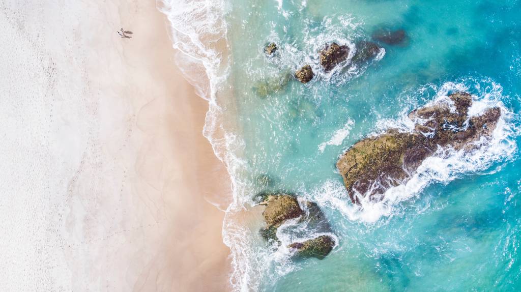 michele-marri-vviT7wFgcSI-unsplash Foto aérea que mostra a areia banhada pelas águas verdes do mar, com algumas pedras