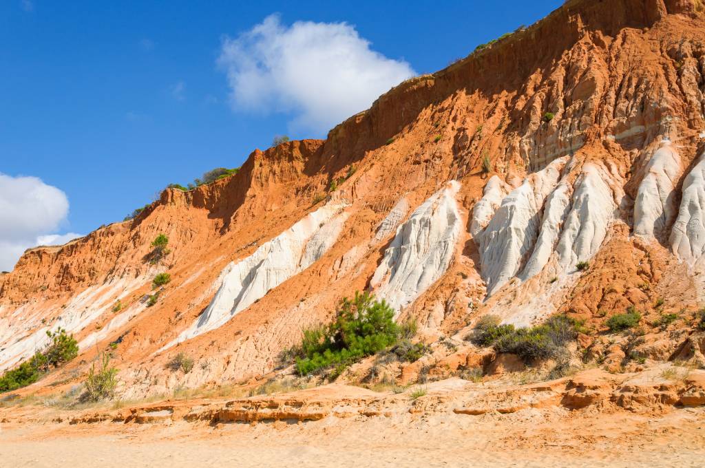 Foto colorida mostra falésias alaranjadas e brancas de quase 40 metros de altura numa praia em Portugal