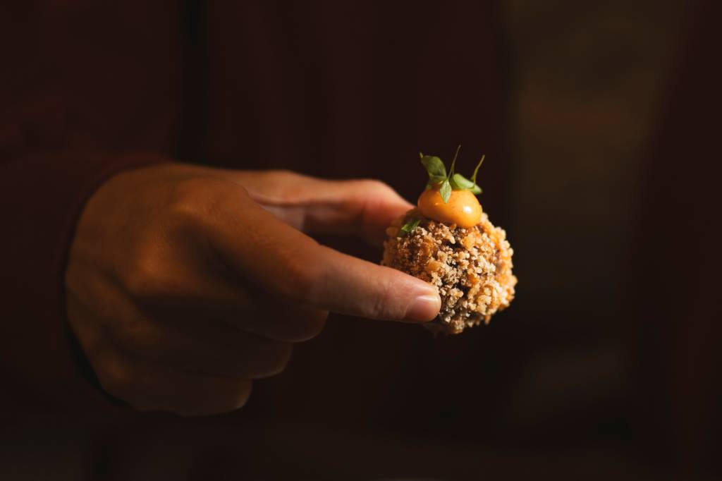 Fotografia colorida mostra uma mão segurando um croquete