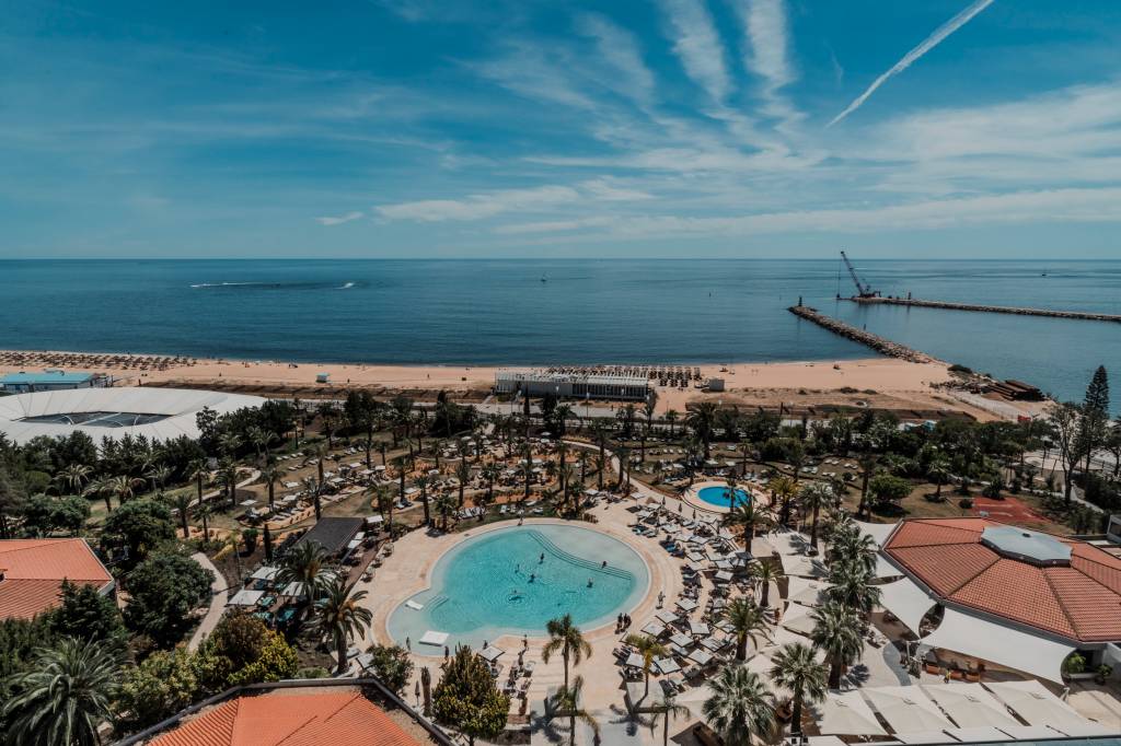 23 Vista do alto mostra o hotel com uma piscina arredondada cercada de coqueiros, com o mar ao fundo