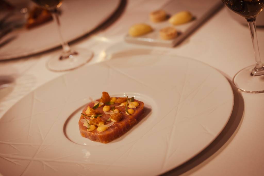 19 2 A imagem mostra detalhe de uma mesa no restaurante do hotel, com um prato de carne decorado com bolinhas de molho e flores no topo