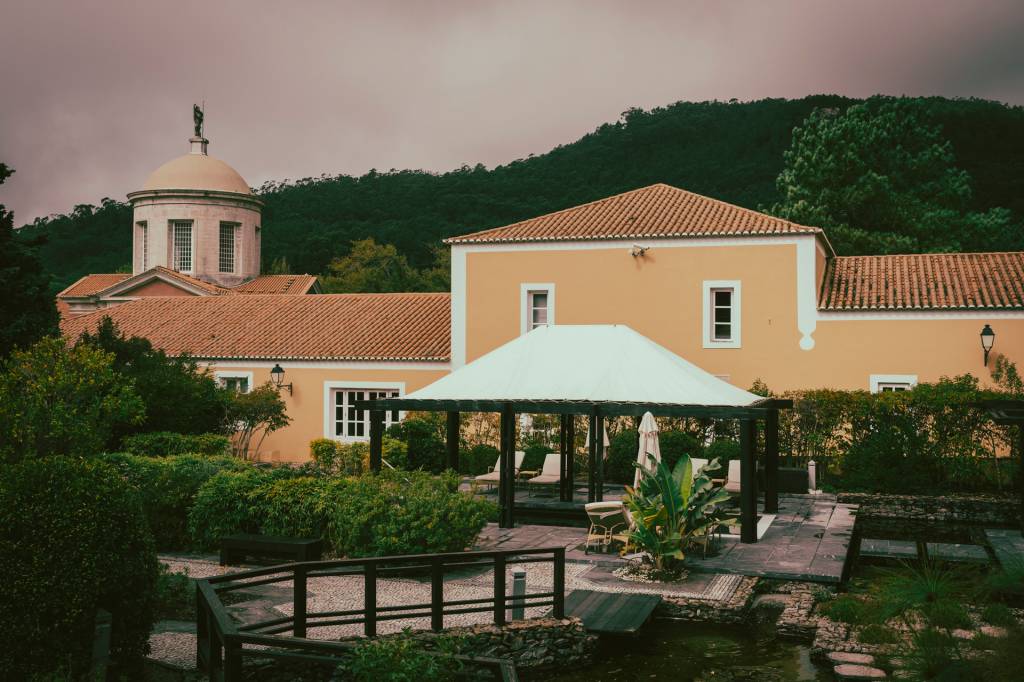 2024_Nuvem-375 Foto mostra as instalações do spa do hotel: um edificio amarelo, com uma torre de igreja ao fundo e a montanha verdejante ao fundo