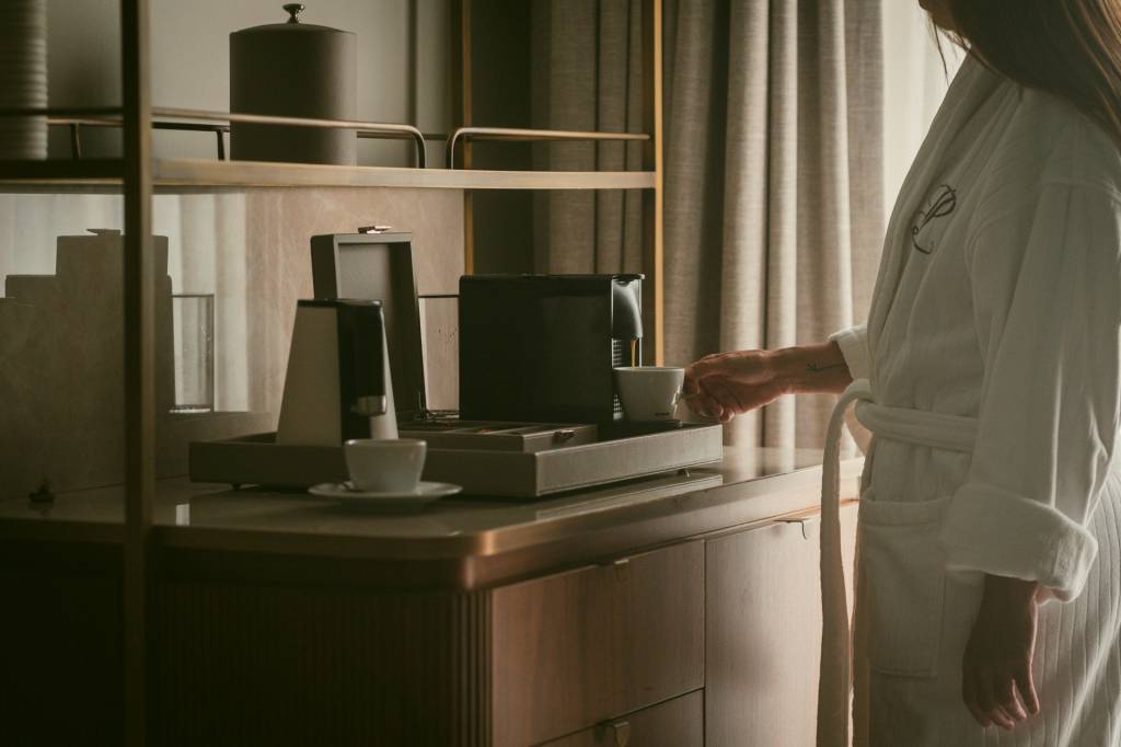 2024_Nuvem-405 2 Detalhe do quarto, com uma pessoa fazendo um café