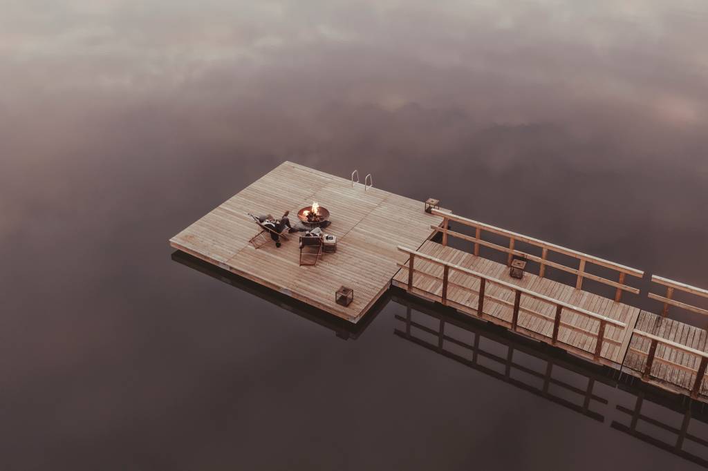 62 2 Imagem aérea mostra um deck de madeira sobre o lago do hotel, com um casal sentado em duas cadeiras em volta de uma fogueira