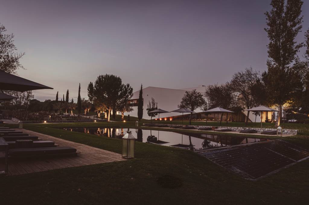 68 2 Imagem mostra o edifício principal do hotel, um caixote branco de linhas retas, com uma piscina em frente e um jardim recheado de árvores