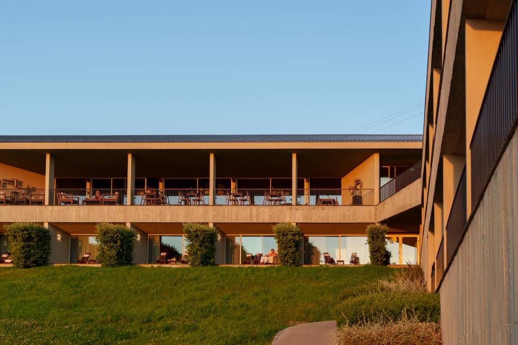 Vista da fachada do hotel, com dois andares de quartos e um gramado na frente