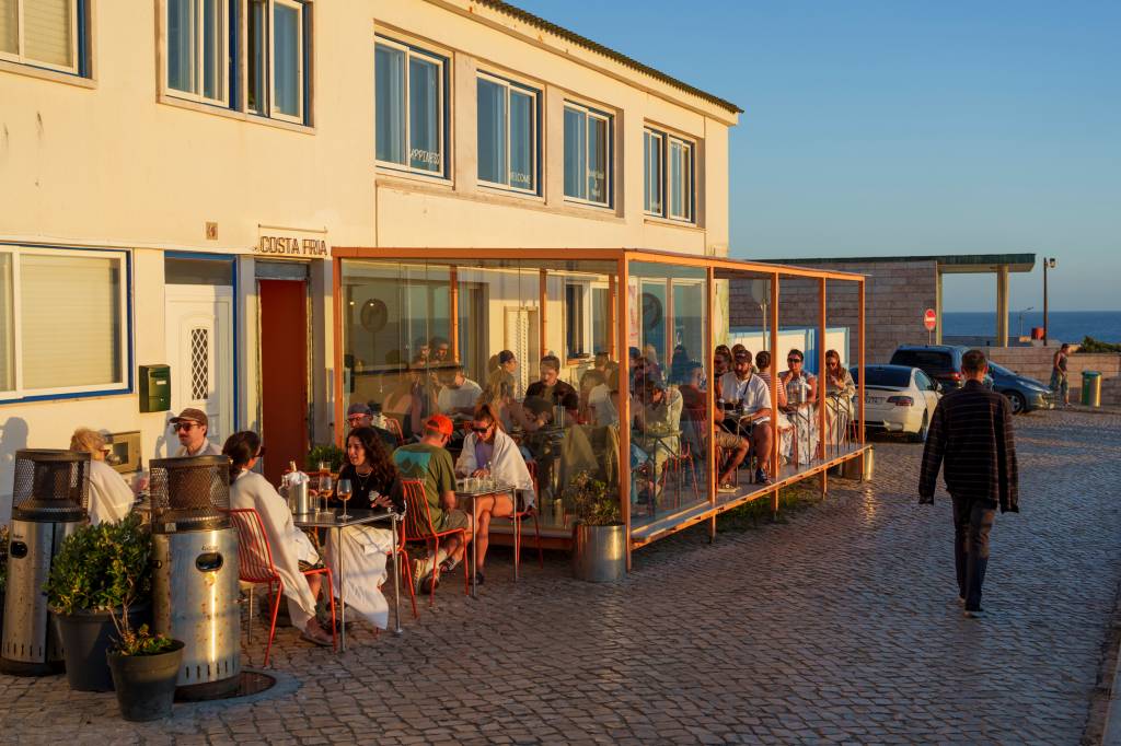 Varanda de um restaurante com mesas lotadas e uma luz de por do sol