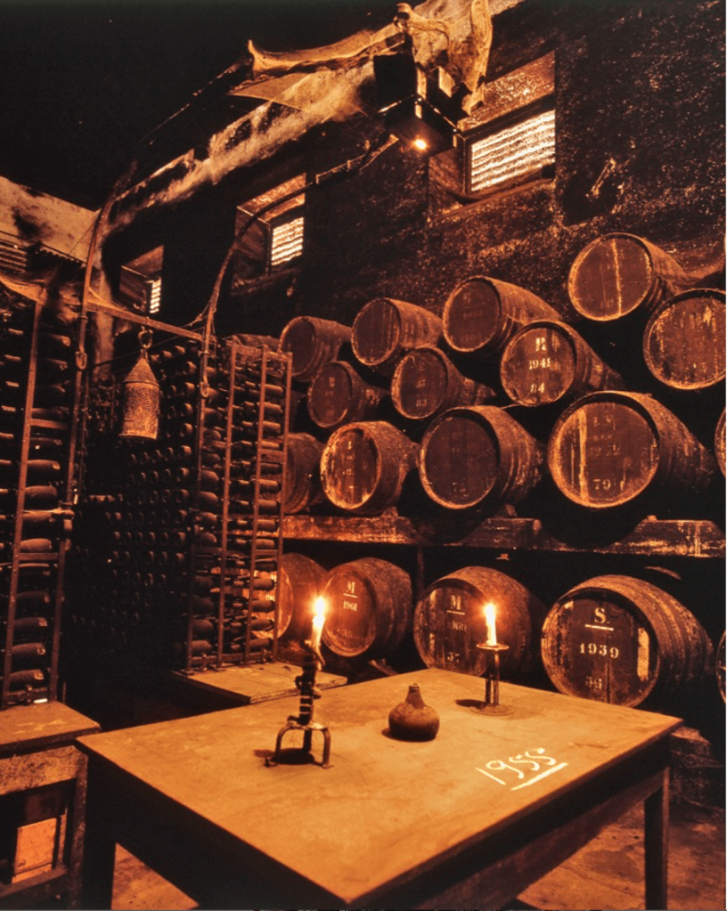 Adega com toneis de vinho e uma mesa, a luz de velas